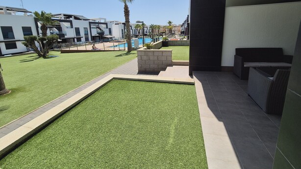Ein moderner Außenbereich mit Kunstgrasanlage, einem Pool und einer Sitzecke mit Tisch und Stühlen.