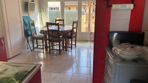 A dining area with a round table and chairs, a television mounted on the wall, and a view of the outside through a glass door. - 3-bedroom house for 6 people (Argelès-sur-Mer)