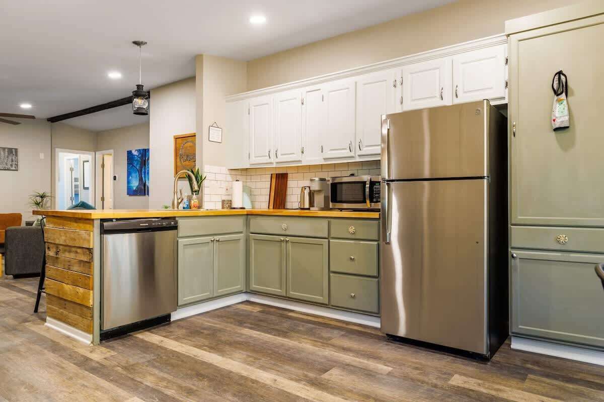A kitchen with a dishwasher, refrigerator, microwave, and wooden countertop.