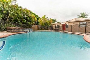Une piscine dont le bord est recouvert de carrelage, entourée d’une clôture et de palmiers.