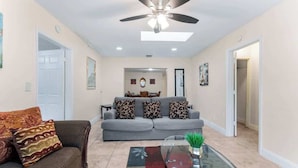 A living room with a grey sofa, a glass coffee table, and a ceiling fan. - 5BR Family Oasis w/ Pool, Near Beach & Downtown (Hollywood)