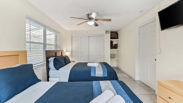 A hotel room with two beds, a ceiling fan, a TV, and a window with blinds. - 5BR Family Oasis w/ Pool, Near Beach & Downtown (Hollywood)