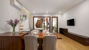 Un comedor moderno con una mesa de madera, dos sillas, un florero con flores y un plato de fruta.
