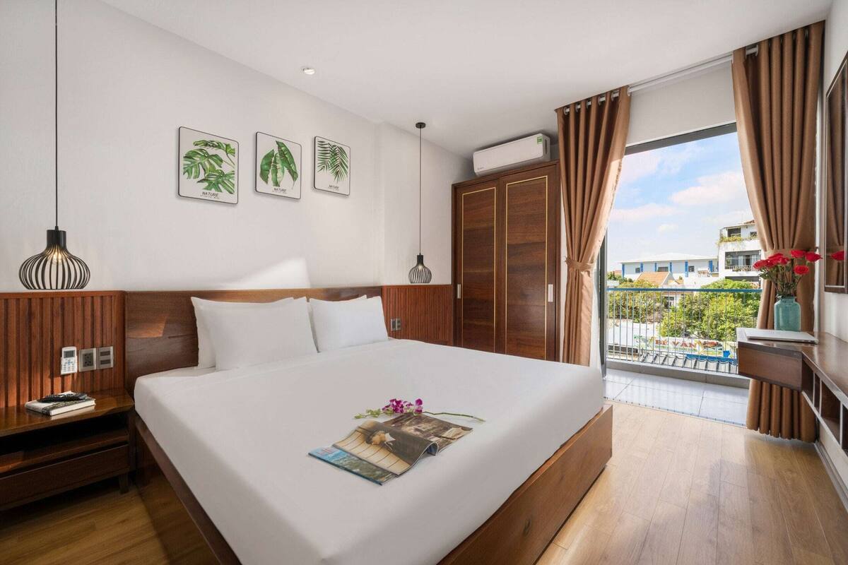 Ein Hotelzimmer mit einem großen Bett, einem Holzkopfteil, einem Nachttisch mit Lampe, einem Kleiderschrank und einem Balkon mit Blick ins Freie.