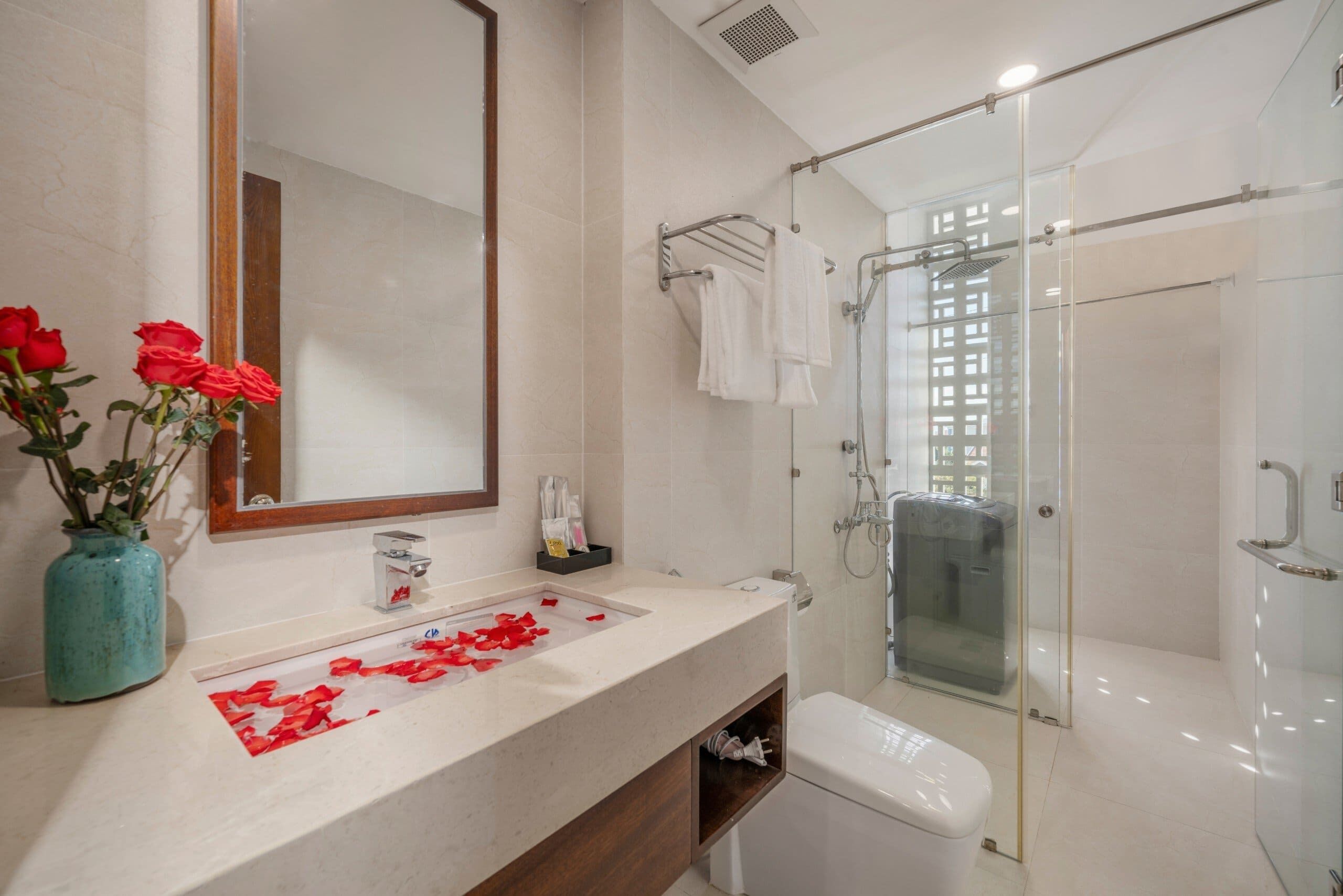 Un baño moderno con un espejo grande, una cabina de ducha de vidrio y un tocador con un lavamanos y un jarrón de rosas rojas.
