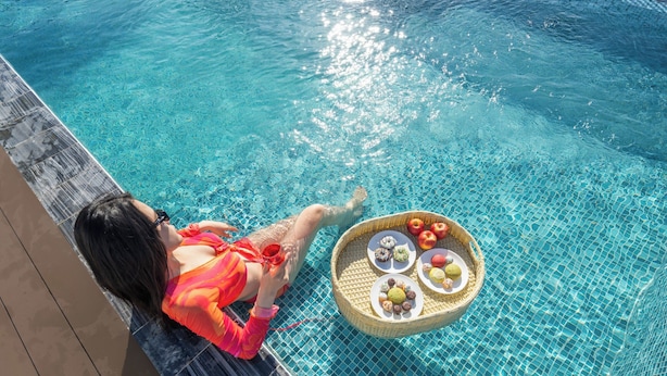 Una persona descansando junto a la piscina con una cesta de aperitivos.