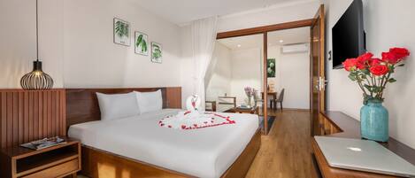 A hotel room with a wooden bed, a nightstand, a laptop, a vase with red roses, and a flat-screen TV.