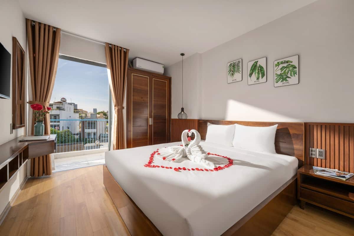 Ein Hotelzimmer mit einem großen Bett, einem Holzkopfteil, einem Nachttisch, einem Fernseher und einem Balkon mit Vorhängen.