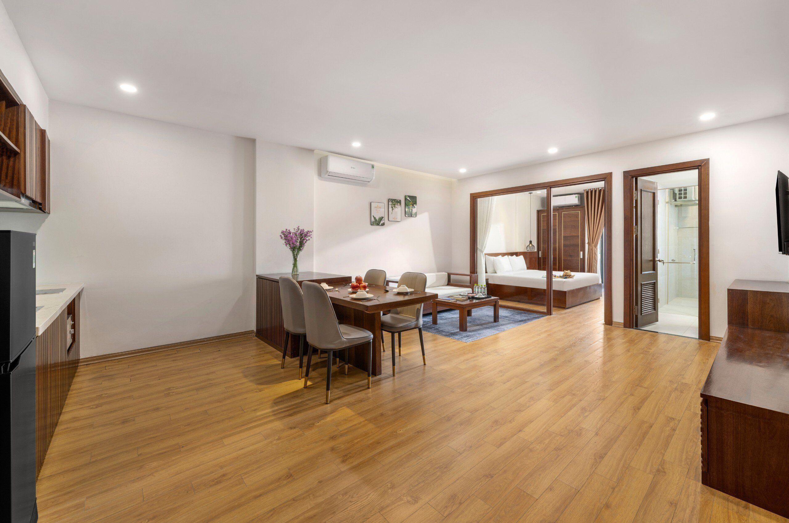 A modern living room with a wooden floor, a dining area with a table and chairs, a sofa, and a TV mounted on the wall.