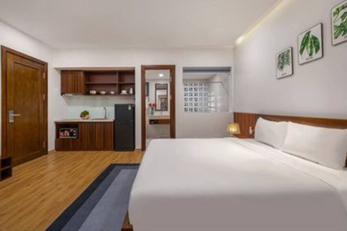 Ein kleines Hotelzimmer mit einem Einzelbett, einer kleinen Küchenzeile und einem durch eine Glastür sichtbaren Badezimmer.