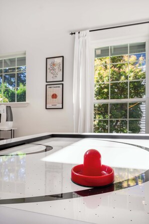 Una habitación con un ventanal grande, una pared blanca con dos obras de arte enmarcadas y un objeto rojo sobre una superficie reflectante.