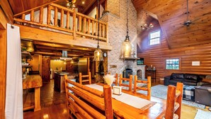 Interior rústico de una cabaña con comedor de madera, chimenea y acogedor salón con sofá de cuero.
