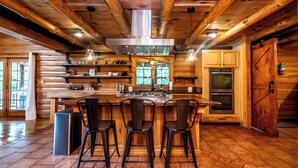 Una cocina rústica con vigas de madera, una isla central con taburetes de bar, electrodomésticos de acero inoxidable y un amplio ventanal.