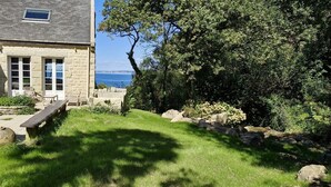 A stone house with a grassy yard, a wooden bench, and a view of the sea. - Magnificent house sea view- Jacuzzi- 2Ha land- GR34 (Poullan-sur-Mer)