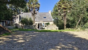 A stone building with a gravel driveway, surrounded by trees and greenery. - Magnificent house sea view- Jacuzzi- 2Ha land- GR34 (Poullan-sur-Mer)