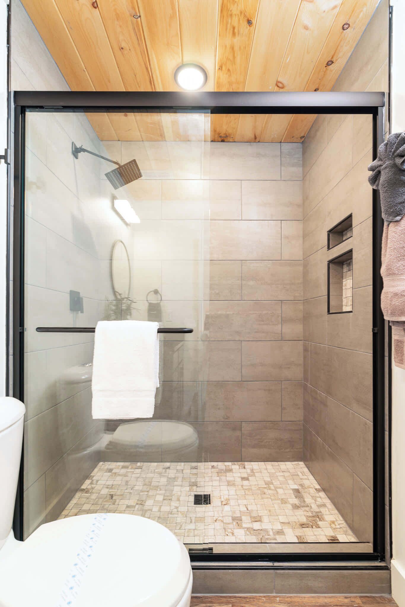 A modern bathroom with a glass-enclosed shower, a toilet, and a wooden ceiling.