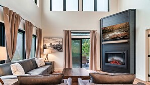 A modern living room with a fireplace, leather sofas, and a large window with curtains.