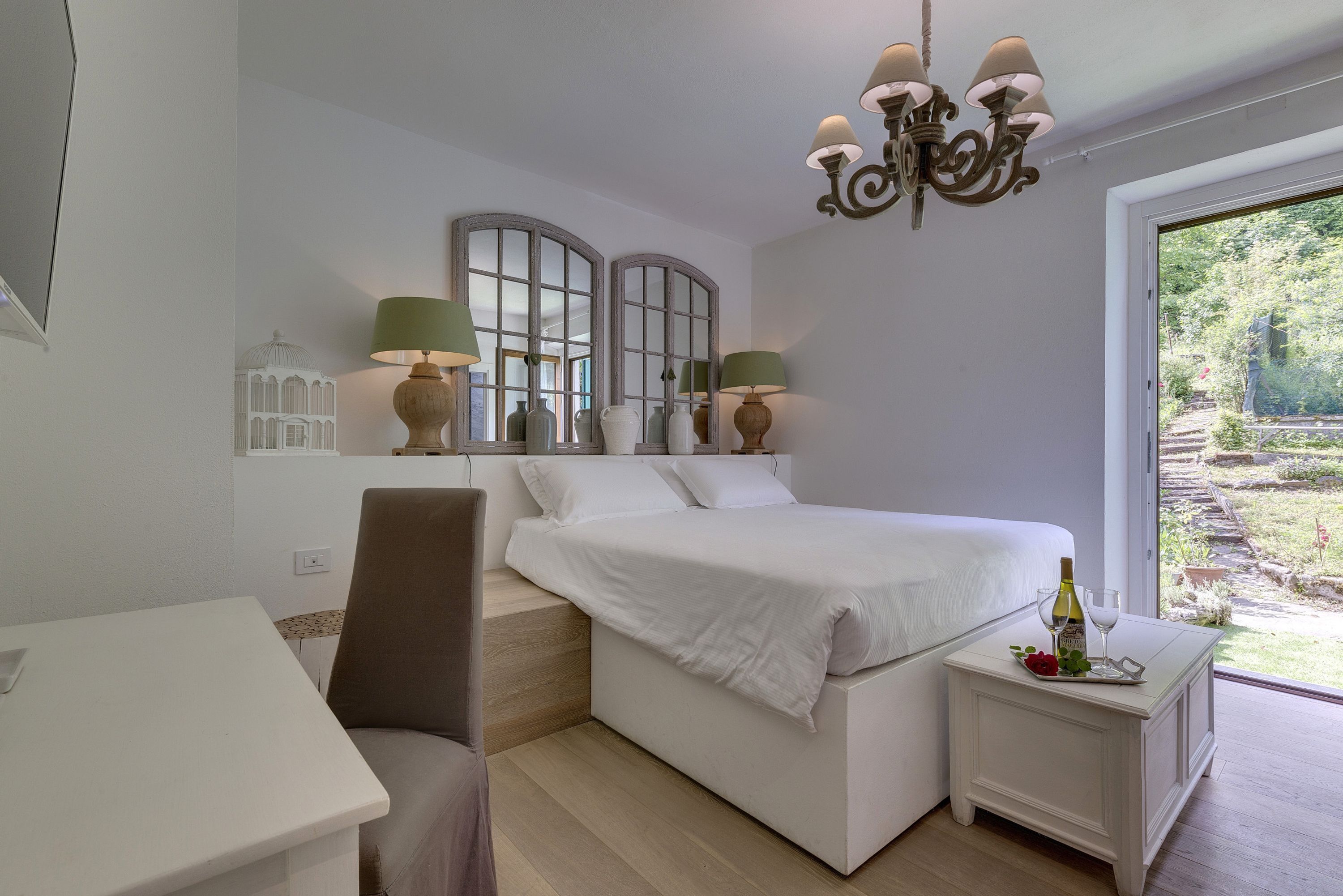 A bedroom with a bed, bedside table, lamp, and a view of the garden.