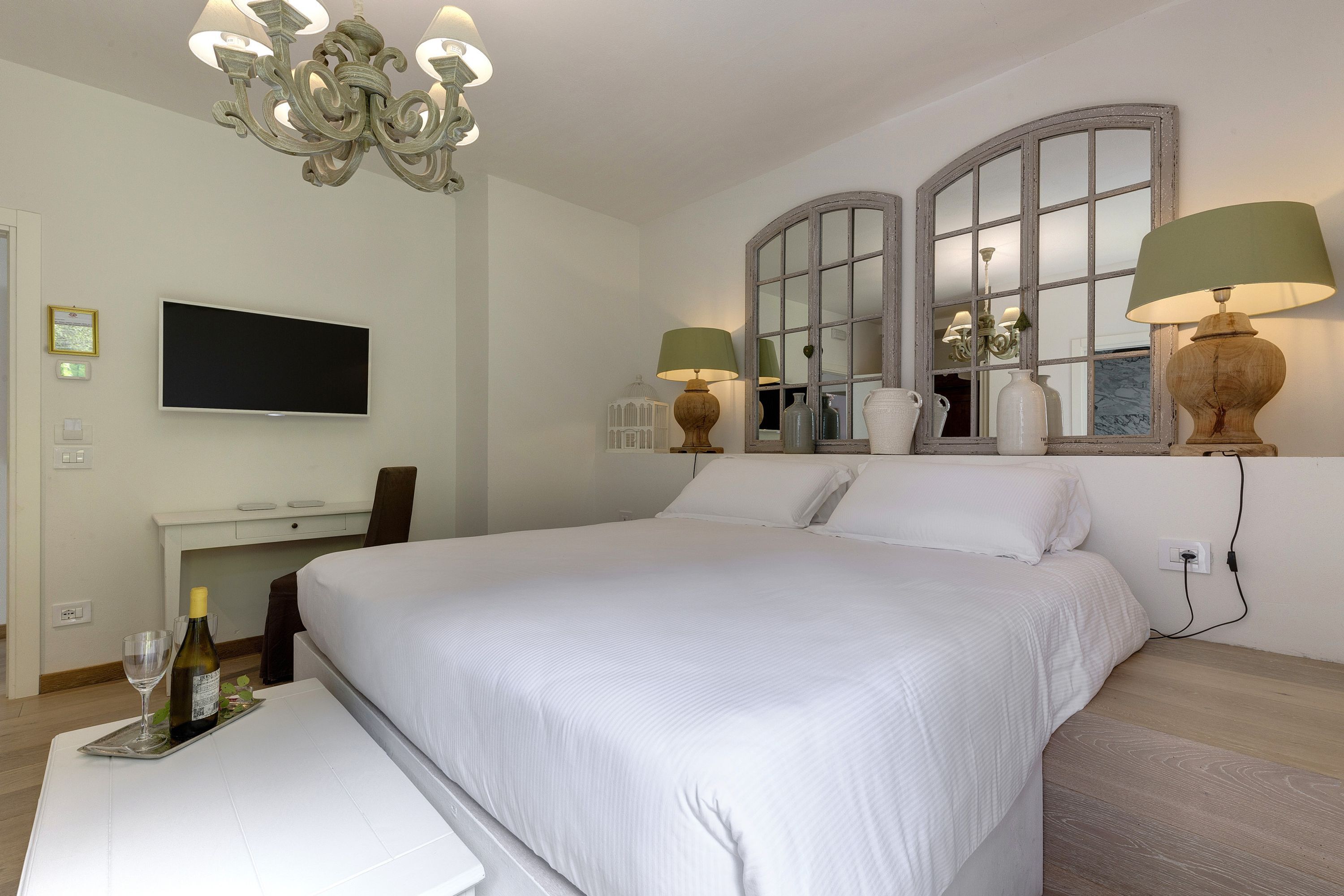 A hotel room with a large bed, a desk, a television, and a chandelier.
