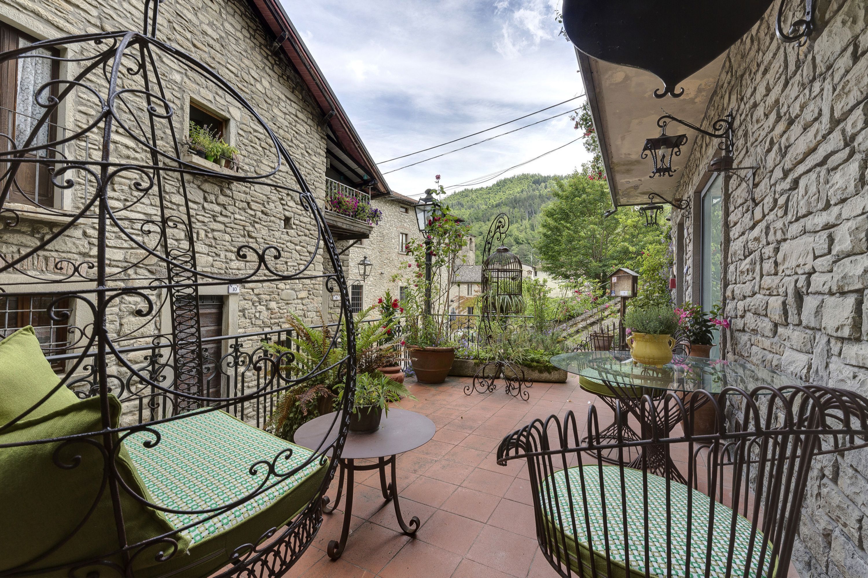 A stone building with a balcony, a small table with chairs, and potted plants.
