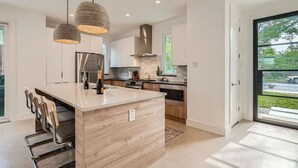 A modern kitchen with a central island, stainless steel appliances, and pendant lighting. - Austin Abode | Heated Pool | Sleeps 12 | Rainey St (Austin)