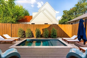 A backyard with a swimming pool, wooden deck, and lounge chairs.