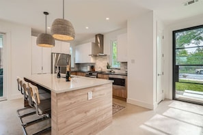 A modern kitchen with a central island, pendant lighting, and a view of the outdoors.