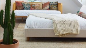 A bedroom with a sloped ceiling, a large window, a cactus, and a bed with multiple pillows. - Austin Abode | Heated Pool | Sleeps 12 | Rainey St (Austin)