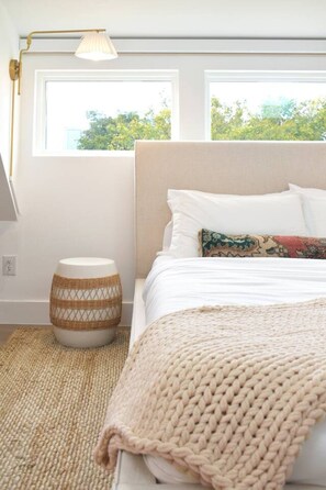 Une chambre à coucher avec un lit, une lampe de chevet, une fenêtre et un tabouret en osier.