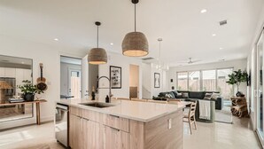 A modern kitchen with a central island, pendant lighting, and a dining area with a sofa. - Austin Abode | Heated Pool | Sleeps 12 | Rainey St (Austin)