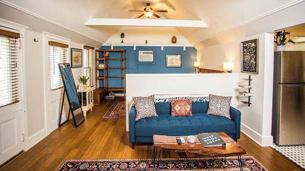 Ein gemütliches Wohnzimmer mit einem blauen Sofa, Holzboden und einem Deckenventilator.