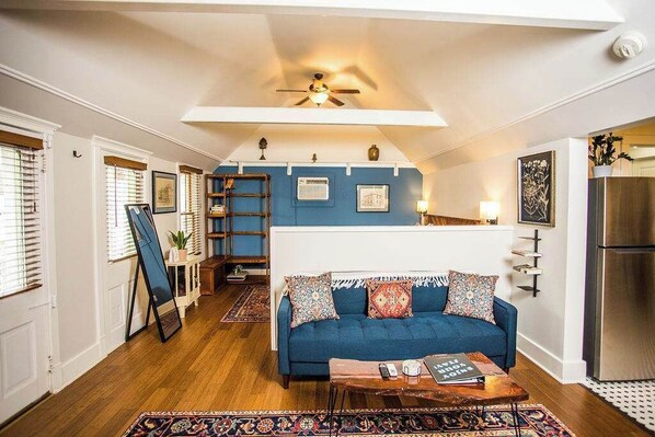 A cozy living room with a blue sofa, wooden flooring, and a ceiling fan.