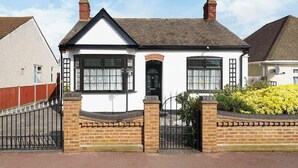 A white house with a black roof, a brick entrance, and a gated driveway. - Charming 3-Bedroom Bungalow in London (Greater London)
