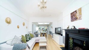 A modern living room with a sofa, a fireplace, and a television. - Charming 3-Bedroom Bungalow in London (Greater London)