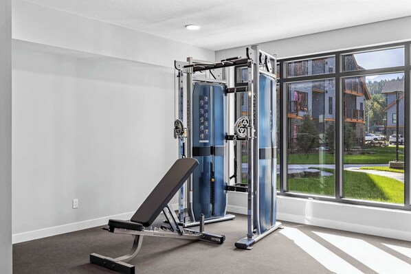 Un gimnasio con equipo de ejercicio y amplios ventanales con vistas a una zona residencial.