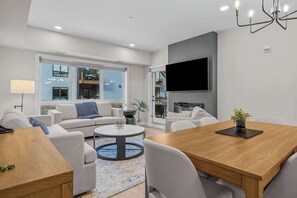 A modern living room with a sofa, a dining table, and a TV mounted on the wall.