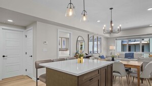 Une cuisine moderne dotée d’un îlot central, de luminaires suspendus et donnant sur l’espace de vie.