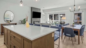 Una cocina moderna con una isla grande, comedor con sillas y un televisor montado en la pared.