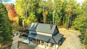 A two-story cabin with a metal roof, surrounded by dense forest. - Spa and Nature | Chalet des Pins Rouge (Sainte-Euphémie-sur-Rivière-Sud)