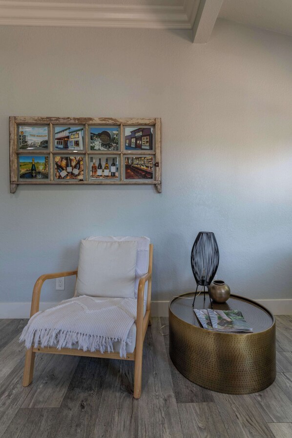A room with a wooden chair, a round table with a vase, and a wall-mounted artwork.