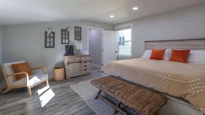 Een slaapkamer met een bed, een stoel, een dressoir en een raam.