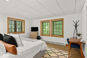 A bedroom with a bed, two windows, a TV, a desk with a plant, and a chair. - Disciples Village #377 Condo | Walking Distance to the Slopes! (Boyne Falls)