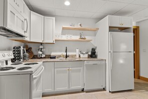 A modern kitchen with white cabinets, a stove, dishwasher, and a refrigerator. - Disciples Village #377 Condo | Walking Distance to the Slopes! (Boyne Falls)