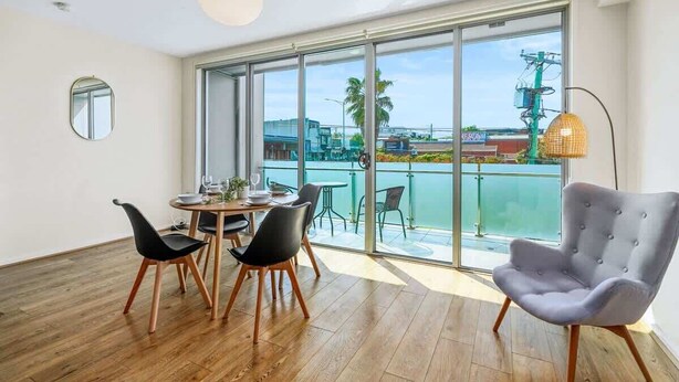 A modern dining area with a round table, four chairs, and a large window overlooking a balcony.