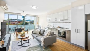 A modern apartment with a kitchen, dining area, and a balcony with a view of a bridge.