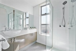 Une salle de bain moderne avec une douche à parois de verre, un grand miroir et un lavabo blanc.