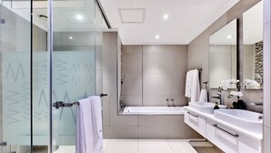 A modern bathroom with a glass shower enclosure, a bathtub, and two sinks with vanity cabinets. - Modern 2-bedroom Executive apartment with WiFi, in Masingita Towers Sandton (Sandton)