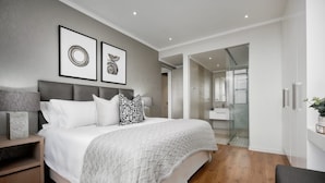 A modern bedroom with a large bed, bedside tables, a nightstand, and a walk-in closet. - Modern 2-bedroom Executive apartment with WiFi, in Masingita Towers Sandton (Sandton)