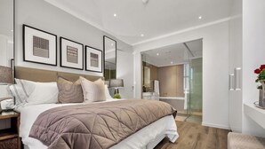 A modern bedroom with a large bed, a nightstand, a bedside table, and a mirror. There are framed pictures on the wall and a door leading to a bathroom. - Modern 2-bedroom Executive apartment with WiFi, in Masingita Towers Sandton (Sandton)