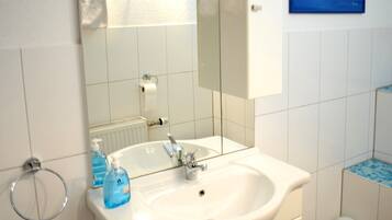 A bathroom with a white sink, a mirror, a toilet, and a blue-tiled shower area.